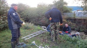 Malcolm, Brian and Bob ponder an 'engineering' solution to getting the heavy water-filled sofa up a seven foot vertical drop. A combo of grappling hook and a lasso arrangement eventually did the trick. (Photo: Ron Pearson)